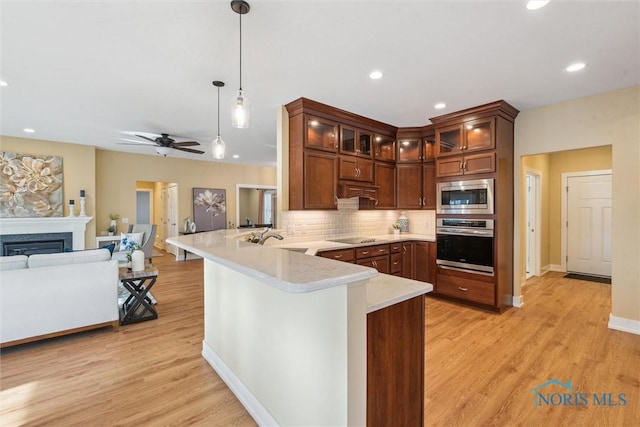 kitchen with a fireplace, stainless steel appliances, light countertops, open floor plan, and a peninsula