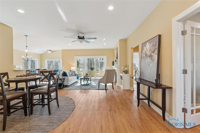 dining room with ceiling fan with notable chandelier, vaulted ceiling, light wood-style flooring, and recessed lighting