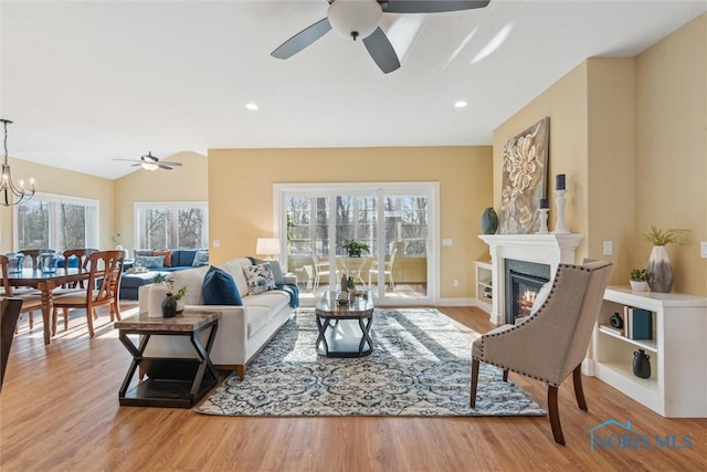 living room featuring a glass covered fireplace, lofted ceiling, wood finished floors, ceiling fan with notable chandelier, and recessed lighting