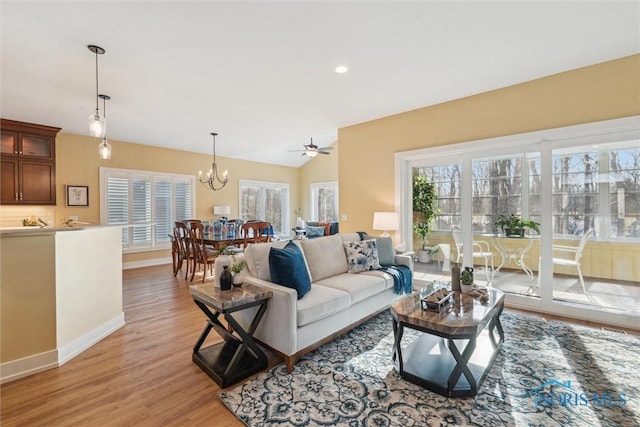 living room with light wood finished floors, recessed lighting, baseboards, lofted ceiling, and ceiling fan with notable chandelier