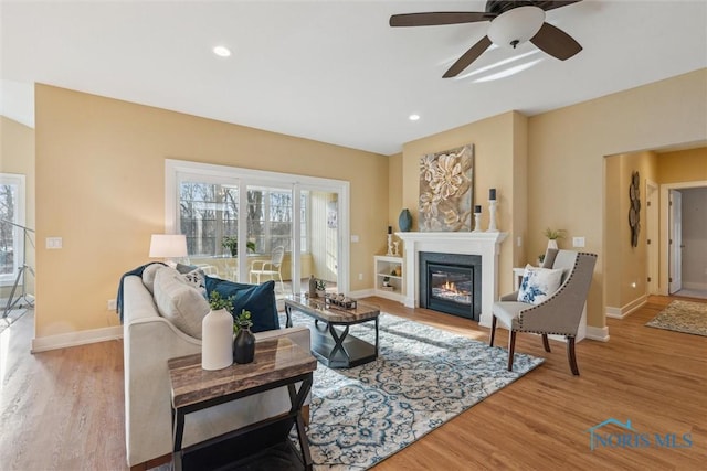 living room featuring a glass covered fireplace, recessed lighting, wood finished floors, and baseboards