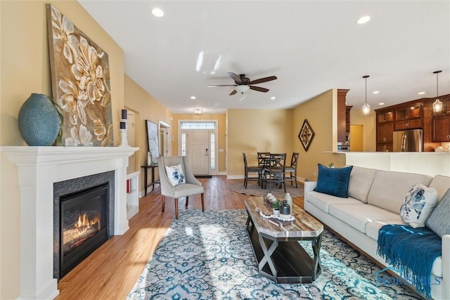 living room featuring baseboards, a glass covered fireplace, ceiling fan, light wood-type flooring, and recessed lighting