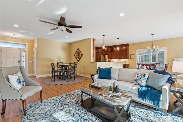 living room with light wood-style floors, recessed lighting, baseboards, and ceiling fan with notable chandelier