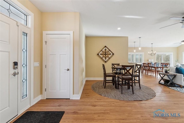 foyer featuring light wood-type flooring, baseboards, and ceiling fan with notable chandelier