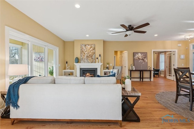 living room featuring ceiling fan, recessed lighting, a glass covered fireplace, and light wood-style floors