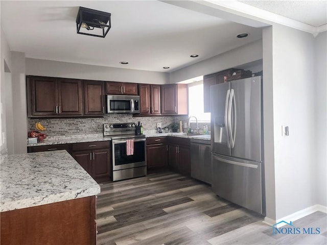 kitchen with dark brown cabinetry, decorative backsplash, dark wood-style floors, appliances with stainless steel finishes, and a sink