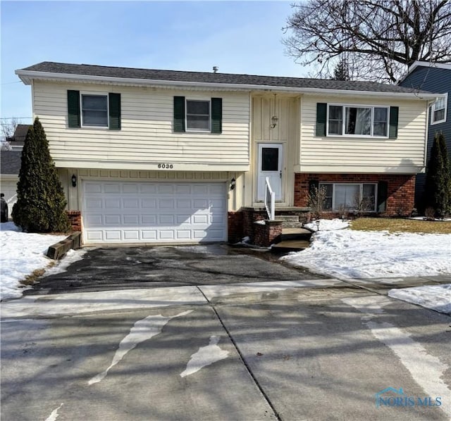 raised ranch featuring entry steps, driveway, brick siding, and an attached garage