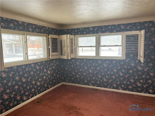 carpeted spare room featuring baseboards, a textured ceiling, visible vents, and wallpapered walls