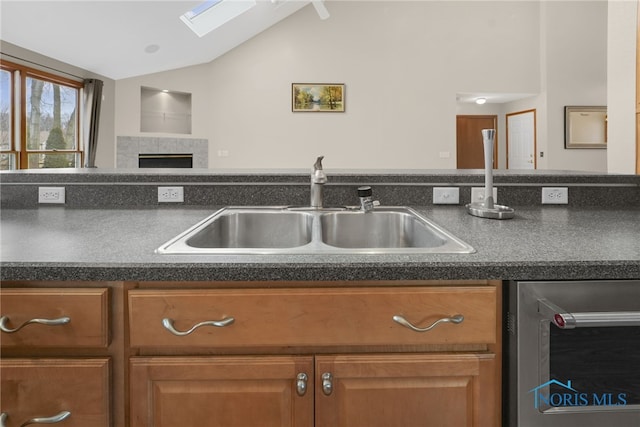 kitchen featuring dark countertops, lofted ceiling with skylight, beverage cooler, and a sink