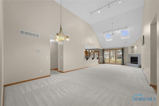 unfurnished living room with a fireplace with raised hearth, light colored carpet, visible vents, baseboards, and track lighting