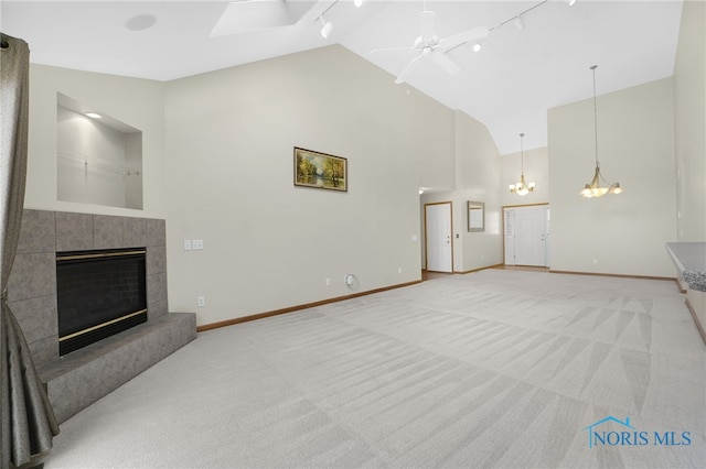 carpeted living area with baseboards, a ceiling fan, a tile fireplace, rail lighting, and high vaulted ceiling