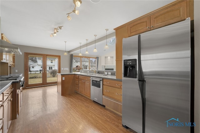 kitchen featuring light wood-style flooring, a peninsula, a sink, appliances with stainless steel finishes, and pendant lighting