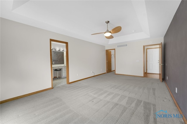 spare room featuring light carpet, a tray ceiling, visible vents, and baseboards