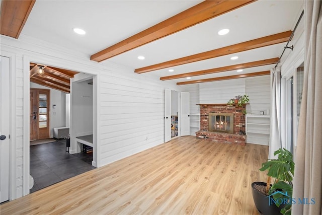 living room featuring a brick fireplace, wood finished floors, beam ceiling, and wooden walls