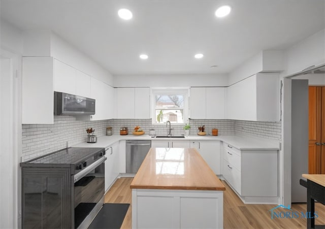 kitchen with appliances with stainless steel finishes, butcher block counters, white cabinetry, and a sink