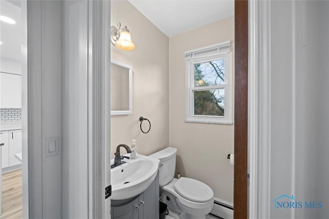 bathroom with tasteful backsplash, toilet, wood finished floors, vanity, and a baseboard heating unit