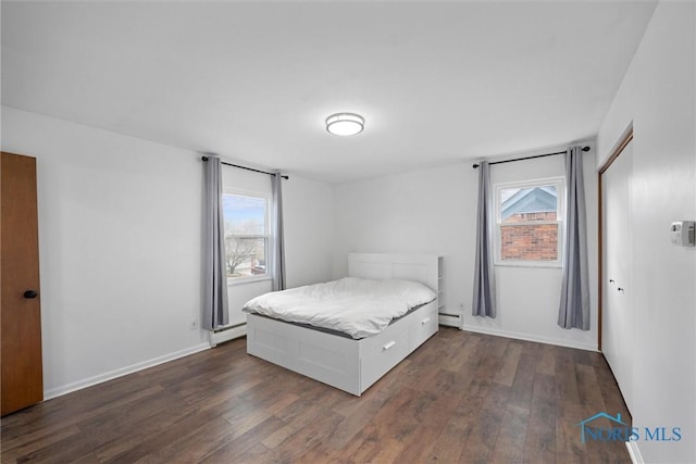 bedroom featuring multiple windows, a baseboard heating unit, and dark wood finished floors