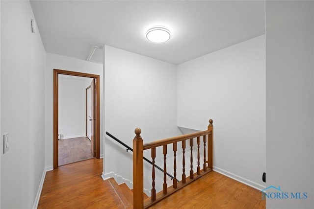 corridor with wood finished floors, an upstairs landing, and baseboards