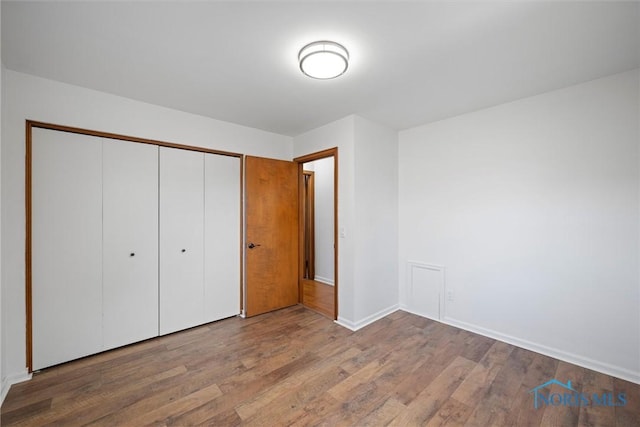 unfurnished bedroom with a closet, wood finished floors, and baseboards