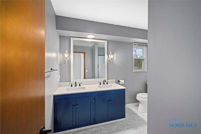 full bathroom with toilet, marble finish floor, double vanity, and a sink