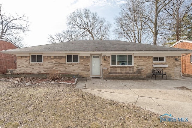 view of front of home with a patio, brick siding, and roof with shingles