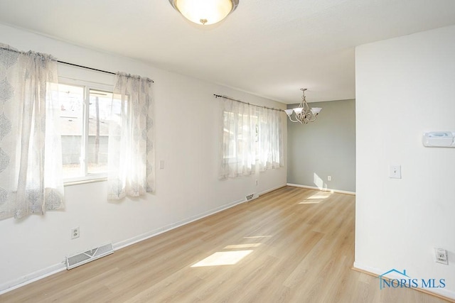 empty room featuring wood finished floors, visible vents, a wealth of natural light, and baseboards