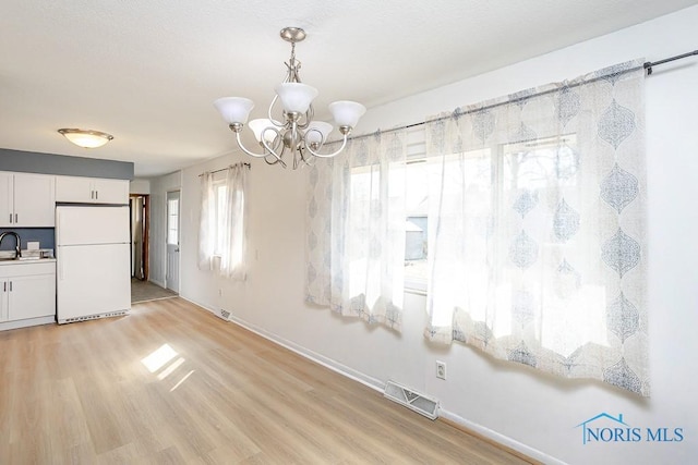 unfurnished dining area featuring visible vents, an inviting chandelier, light wood-type flooring, and baseboards