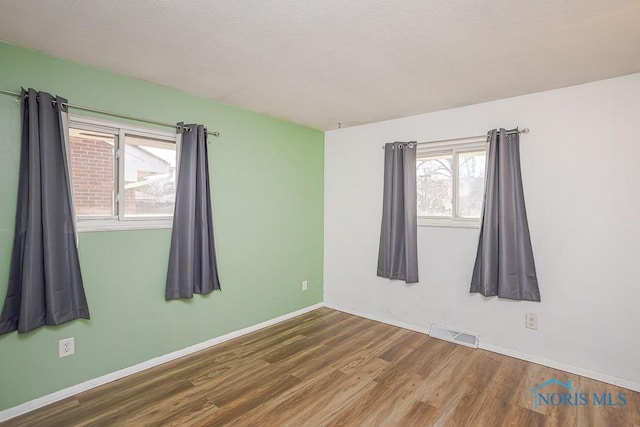 unfurnished room featuring a textured ceiling, wood finished floors, visible vents, and baseboards