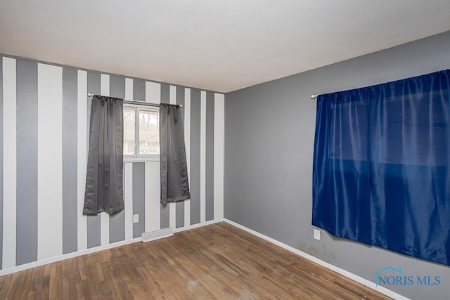 unfurnished room with visible vents, wood finished floors, baseboards, and a textured ceiling