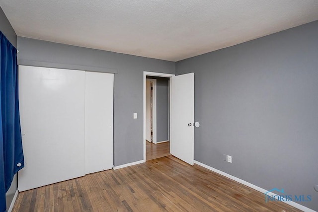 unfurnished bedroom featuring baseboards, wood-type flooring, a textured ceiling, and a closet