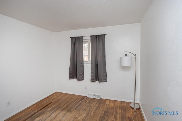 empty room featuring visible vents, baseboards, and hardwood / wood-style flooring