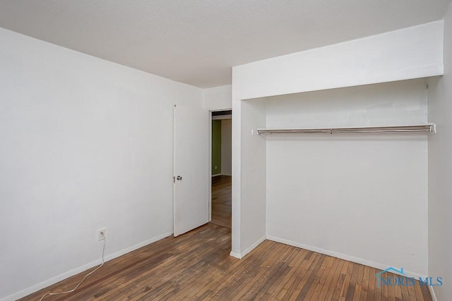 unfurnished bedroom with a closet, baseboards, and hardwood / wood-style floors