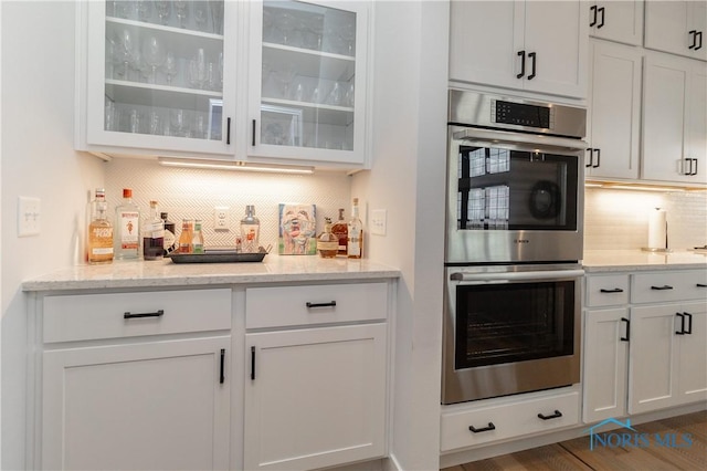 kitchen featuring double oven, white cabinetry, glass insert cabinets, and backsplash