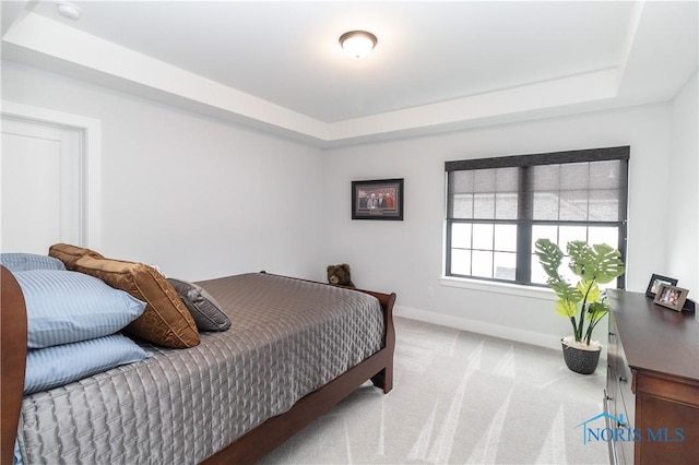 carpeted bedroom with baseboards and a raised ceiling