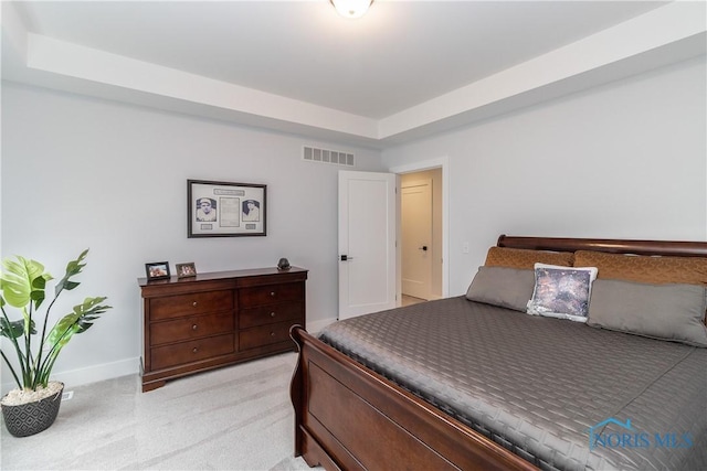 bedroom with light carpet, a tray ceiling, visible vents, and baseboards