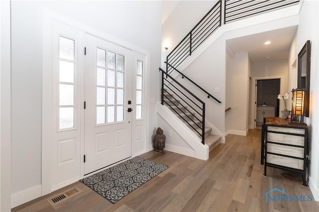 entrance foyer featuring baseboards, visible vents, wood finished floors, a high ceiling, and stairs