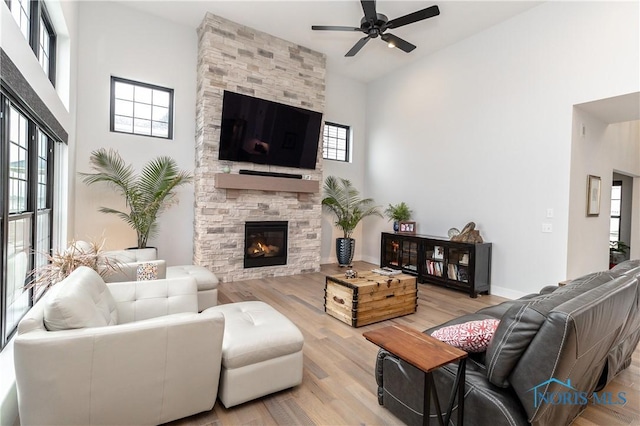 living room featuring a fireplace, a high ceiling, a ceiling fan, wood finished floors, and baseboards