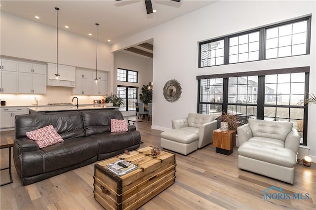 living area featuring a towering ceiling, light wood-type flooring, baseboards, and a ceiling fan