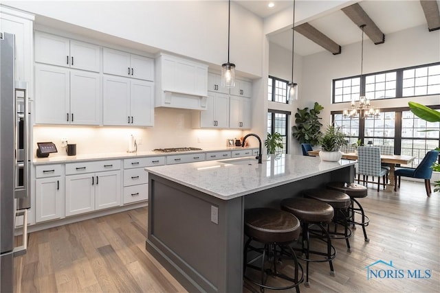 kitchen with a breakfast bar, stainless steel gas cooktop, light wood-style floors, a sink, and beamed ceiling