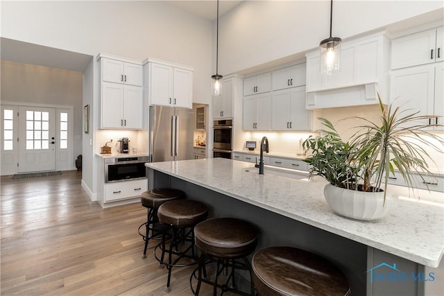 kitchen featuring high quality fridge, a breakfast bar, a towering ceiling, white cabinets, and light wood finished floors