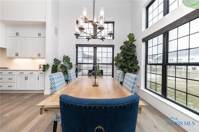 dining space with a towering ceiling, light wood-style flooring, visible vents, and a notable chandelier