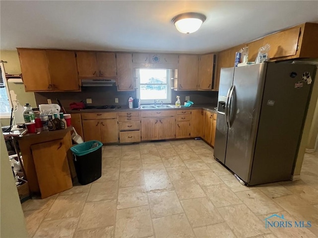 kitchen featuring cooktop, stainless steel refrigerator with ice dispenser, a sink, and under cabinet range hood