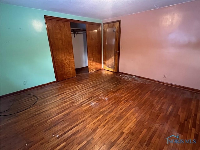 unfurnished bedroom featuring dark wood-style floors, a closet, and baseboards