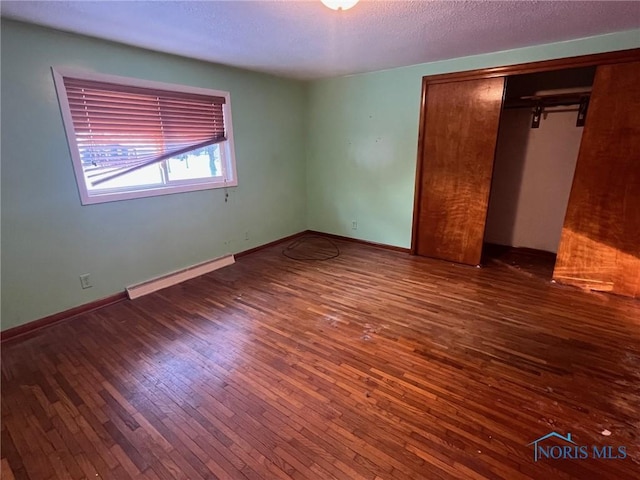 unfurnished bedroom with wood-type flooring, baseboards, baseboard heating, and a closet