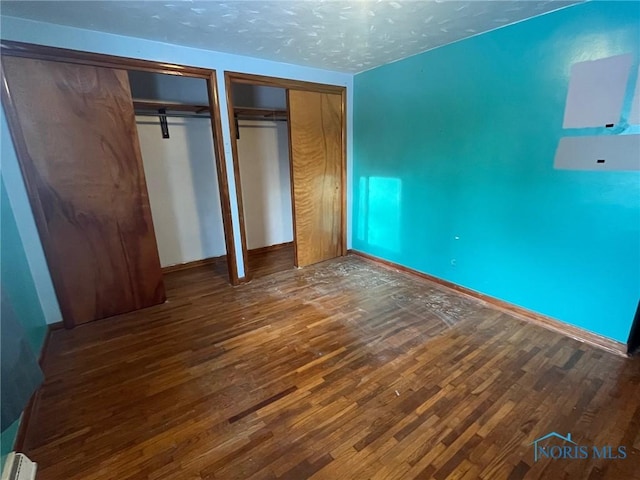 unfurnished bedroom featuring wood finished floors, a textured ceiling, baseboards, and two closets