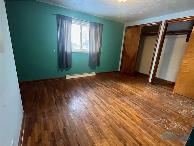 unfurnished bedroom featuring multiple closets, a baseboard radiator, hardwood / wood-style floors, a textured ceiling, and baseboards