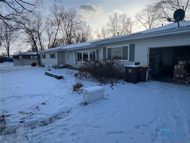 snow covered back of property featuring an attached garage