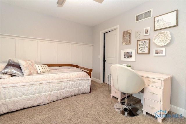 bedroom with visible vents, a ceiling fan, carpet, wainscoting, and a decorative wall