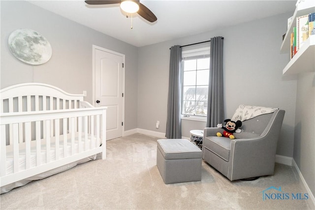 carpeted bedroom featuring baseboards, a crib, and a ceiling fan