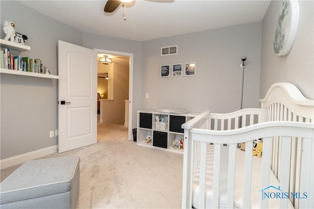 bedroom featuring a nursery area, carpet flooring, visible vents, and ceiling fan